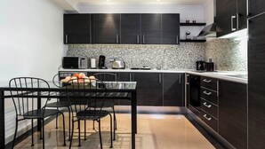 A modern kitchen with dark cabinets, a marble backsplash, and a dining area with a black table and chairs.