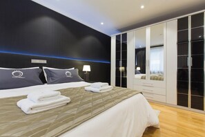 Un dormitorio moderno con una cama grande, un armario con puertas espejadas y una mesita de noche con lámpara.