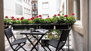 A balcony with two black chairs, a small table, and a potted plant with red flowers.