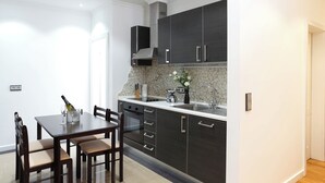 Una cocina moderna con armarios oscuros, horno empotrado y zona de comedor con mesa y sillas.