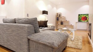Una sala moderna con un sofá gris, una mesa de centro de vidrio y una alfombra blanca.