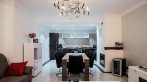 A modern living room with a dining area, a kitchen in the background, and a fireplace.