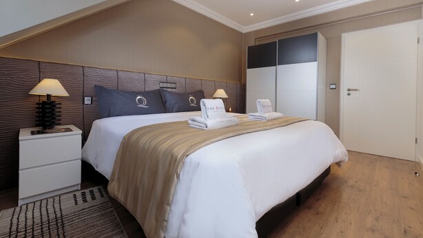 A hotel room with a large bed, two bedside tables, a nightstand, a wardrobe, and a door.