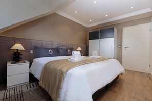 A hotel room with a large bed, two bedside tables, a nightstand, a wardrobe, and a door.