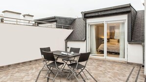 A patio with a table and chairs, a sliding glass door leading to a bedroom, and a white wall with a roof extension.