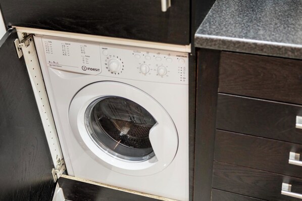 A front-loading washing machine with control panel and a dark wooden cabinet.
