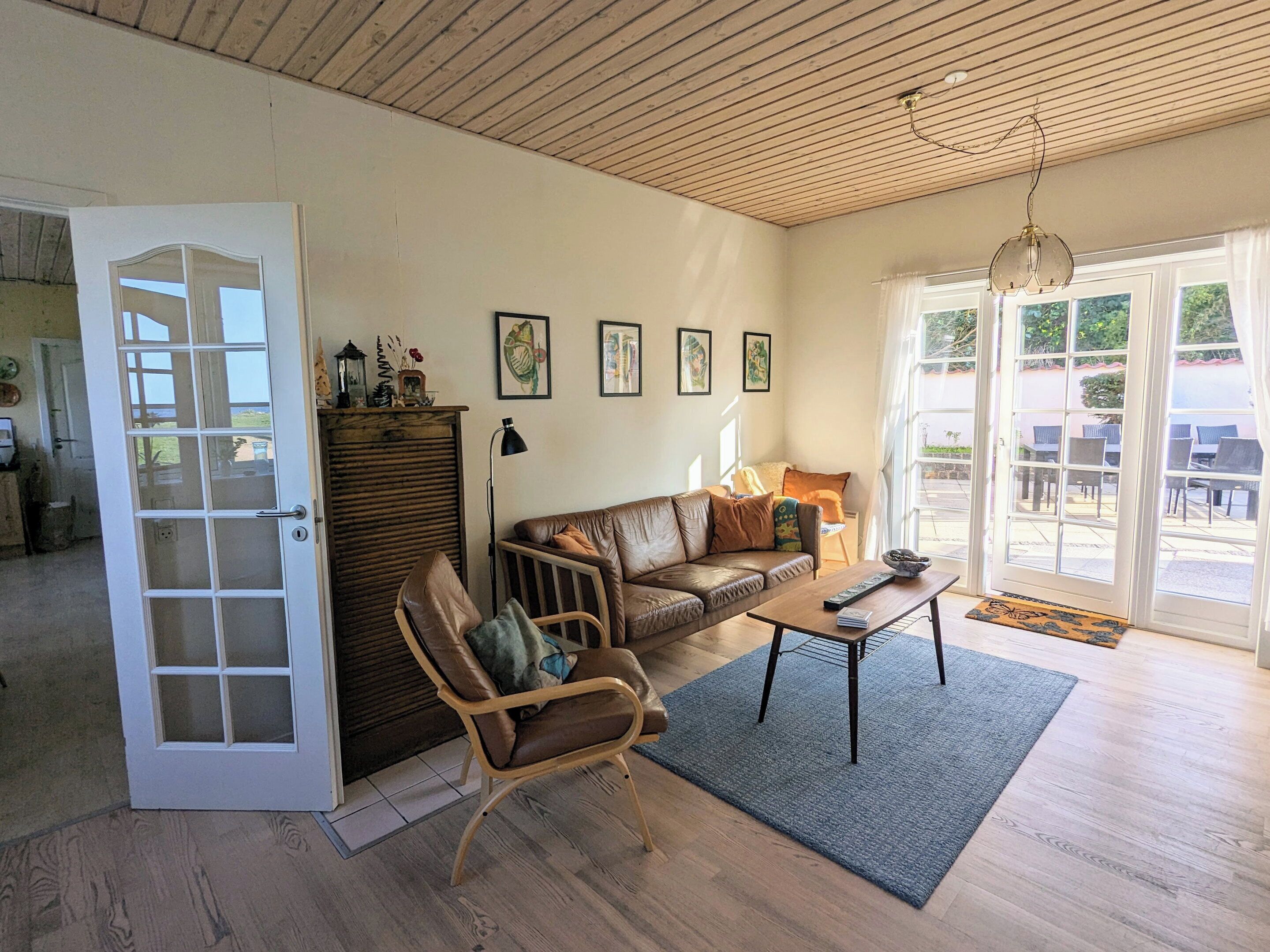 A living room with a wooden ceiling, a sofa, a chair, a coffee table, and a door leading outside.