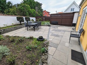 A patio with a table and chairs, surrounded by a stone wall and a wooden fence. - Lovely 2-story cabin by the sea on Bornholm (Svaneke)
