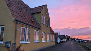 Rivi keltaisia rakennuksia, joissa on punaiset katot, kirkas taivas ja tie, joka johtaa kauas horisonttiin.