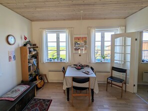A dining area with a table, chairs, a guitar, a bookshelf, and a view through the windows.