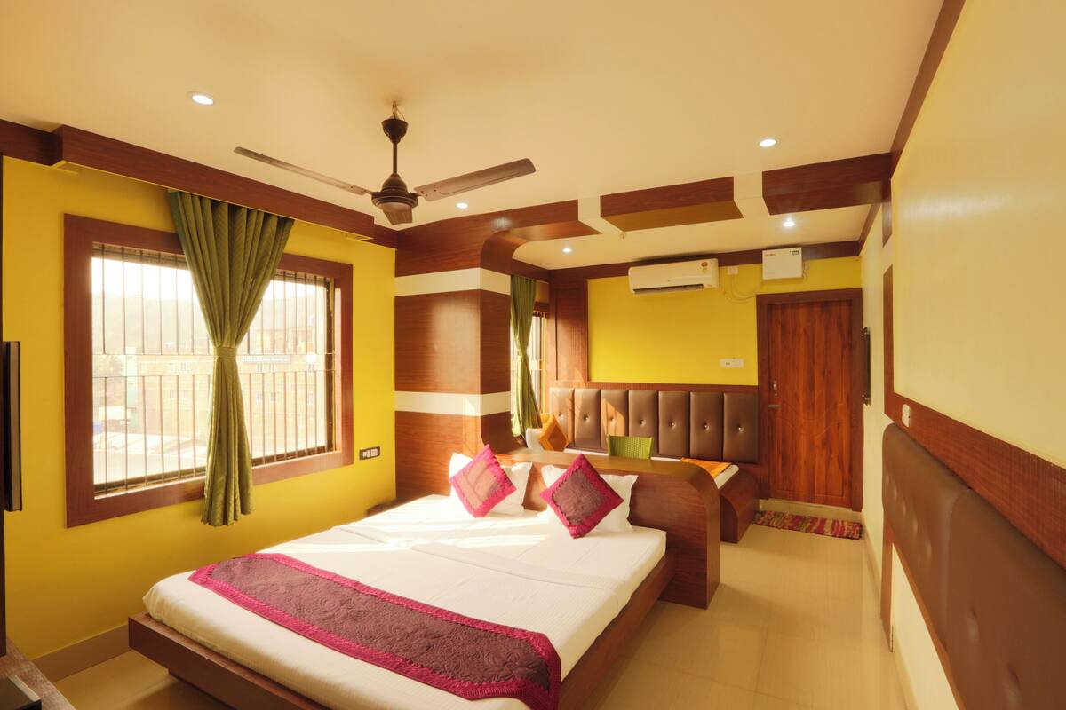Une chambre d’hôtel avec un grand lit, un ventilateur de plafond, un appareil de climatisation et une fenêtre avec des rideaux.