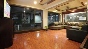 A spacious hotel lobby with a wooden floor, a large sofa, and a television on the left.