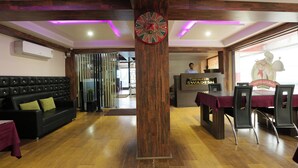 A lobby with a wooden pillar, a reception desk, a black leather sofa, and a dining area with a table and chairs.