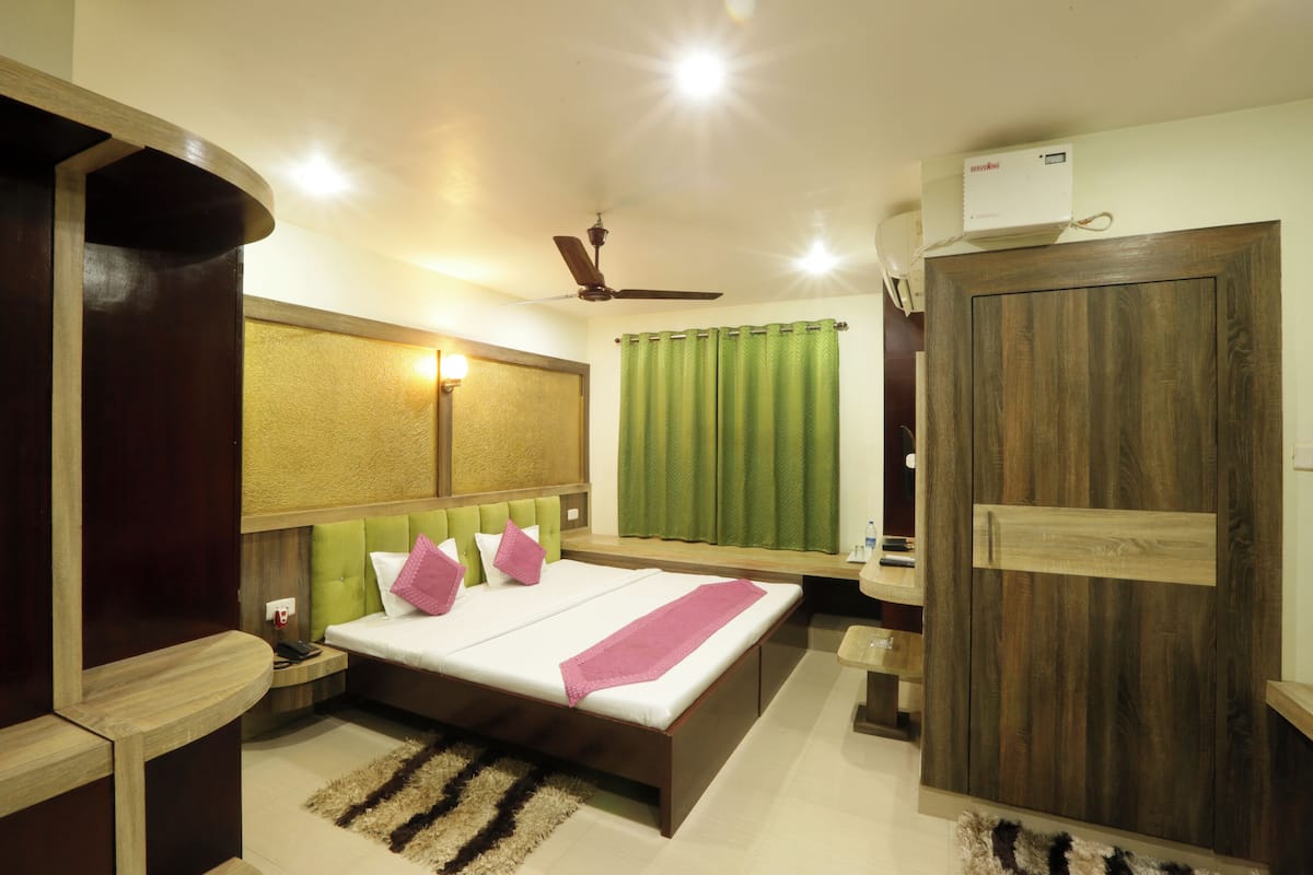 Une chambre à coucher moderne avec un grand lit, un ventilateur de plafond, une armoire en bois et une petite table de chevet.