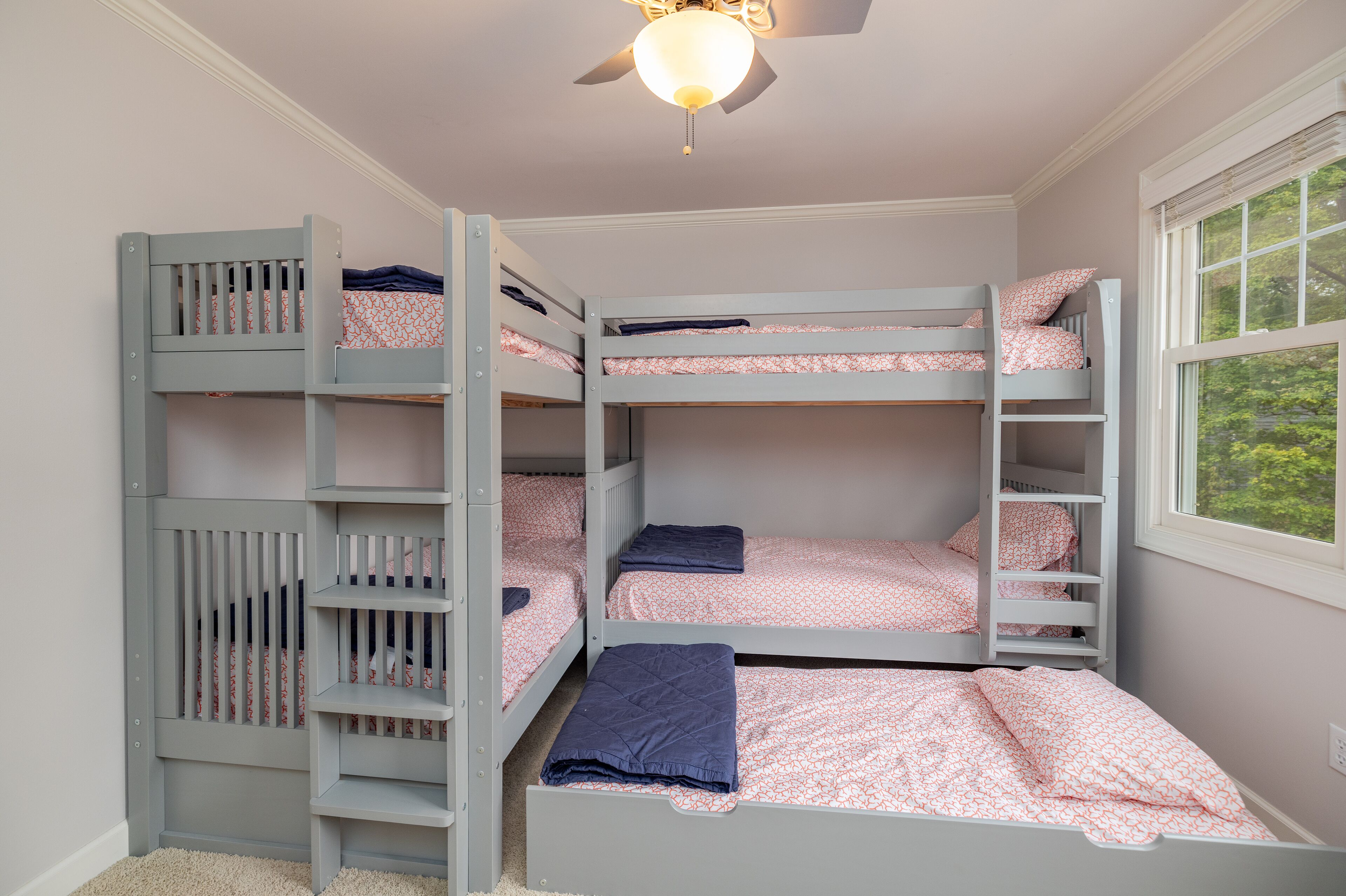 A bunk bed room with a ceiling fan, a window with a view of trees, and a door with a patterned mat.