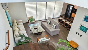 Un salon moderne avec un canapé, une table basse et des fauteuils, un escalier avec des marches en bois, et une vue sur la cuisine et l’espace repas.