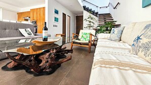 Un salon moderne avec une table basse en verre, une table d’appoint en bois, un canapé et un fauteuil. Un escalier mène à un niveau supérieur.