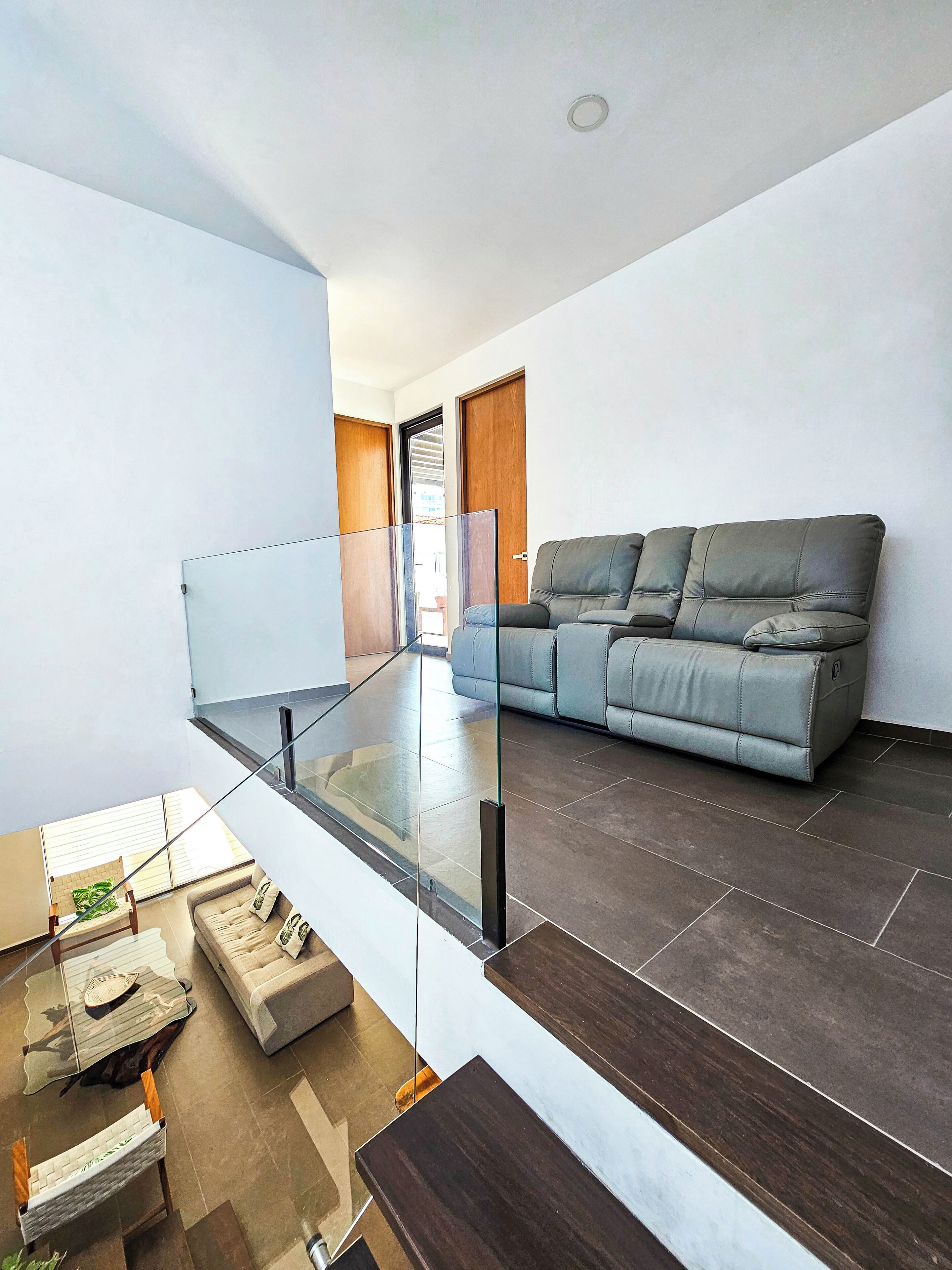 Ein modernes Wohnzimmer mit einem Glasbalkon, einem grauen Sofa und einem Couchtisch.