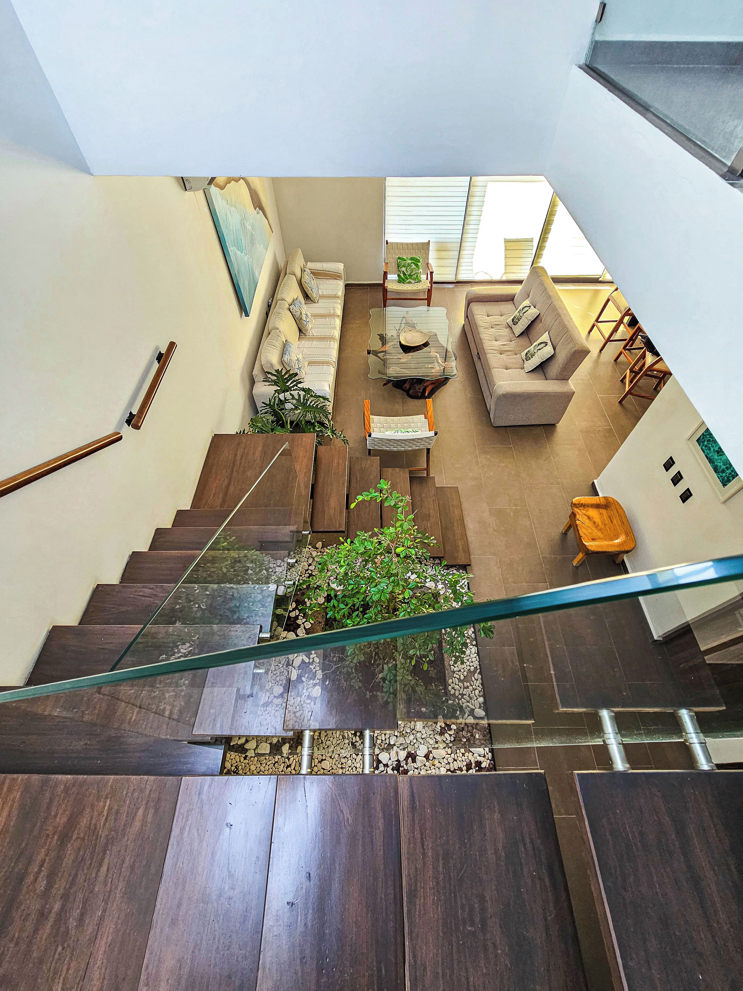 A modern interior with a staircase leading to a living area, featuring a sofa, chairs, and a glass table.
