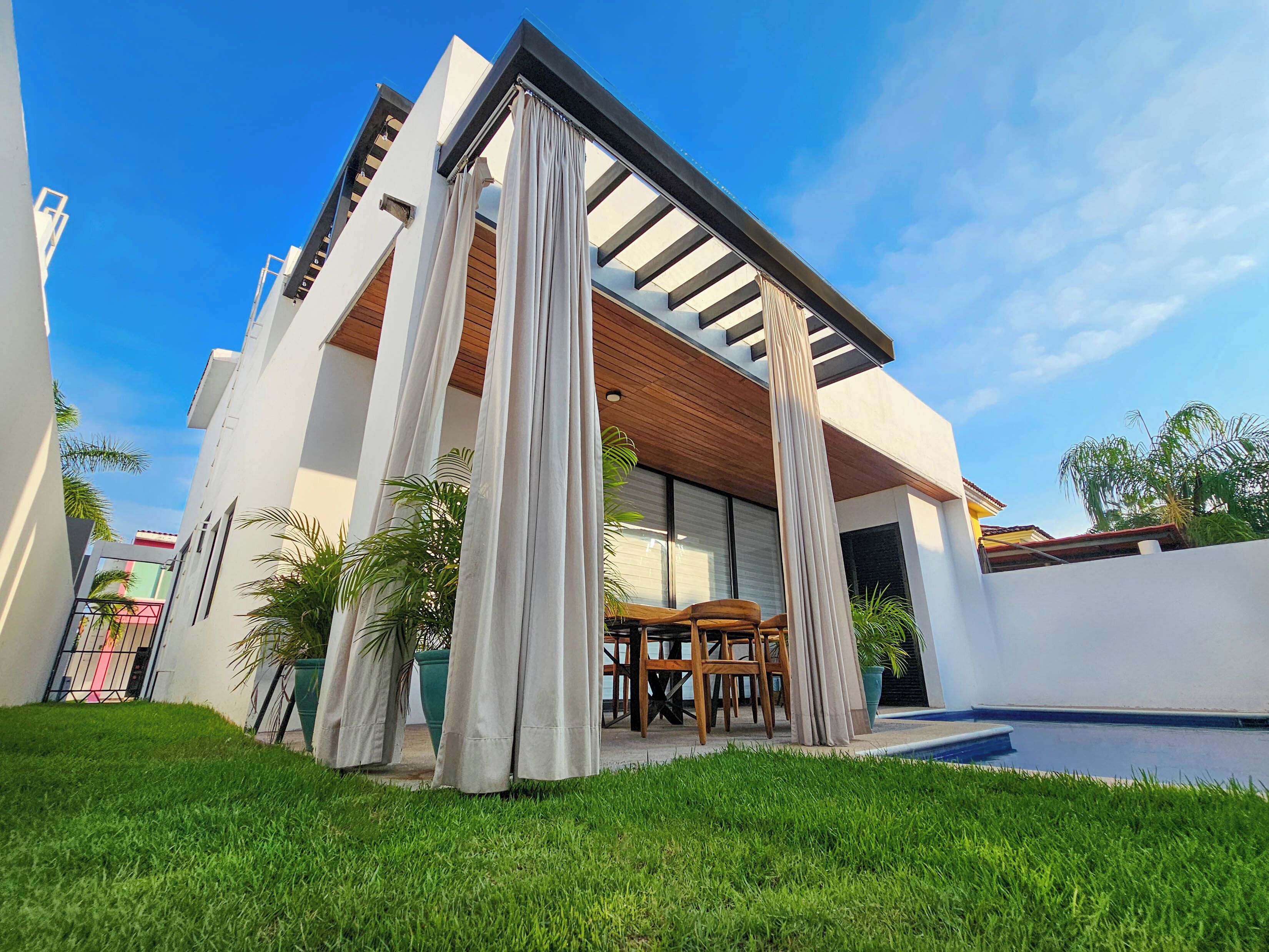 A modern house with a covered patio, a swimming pool, and a well-maintained lawn.