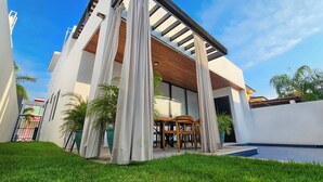 Une maison moderne dotée d’un patio couvert, d’une piscine et d’une pelouse bien entretenue.
