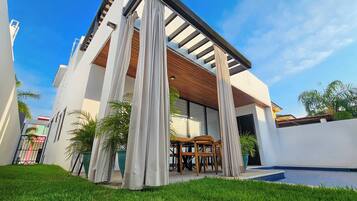 A modern house with a covered patio, a swimming pool, and a well-maintained lawn.