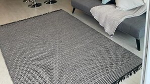 Una sala de estar moderna con un sofá gris, alfombra estampada y estanterías hexagonales en la pared.