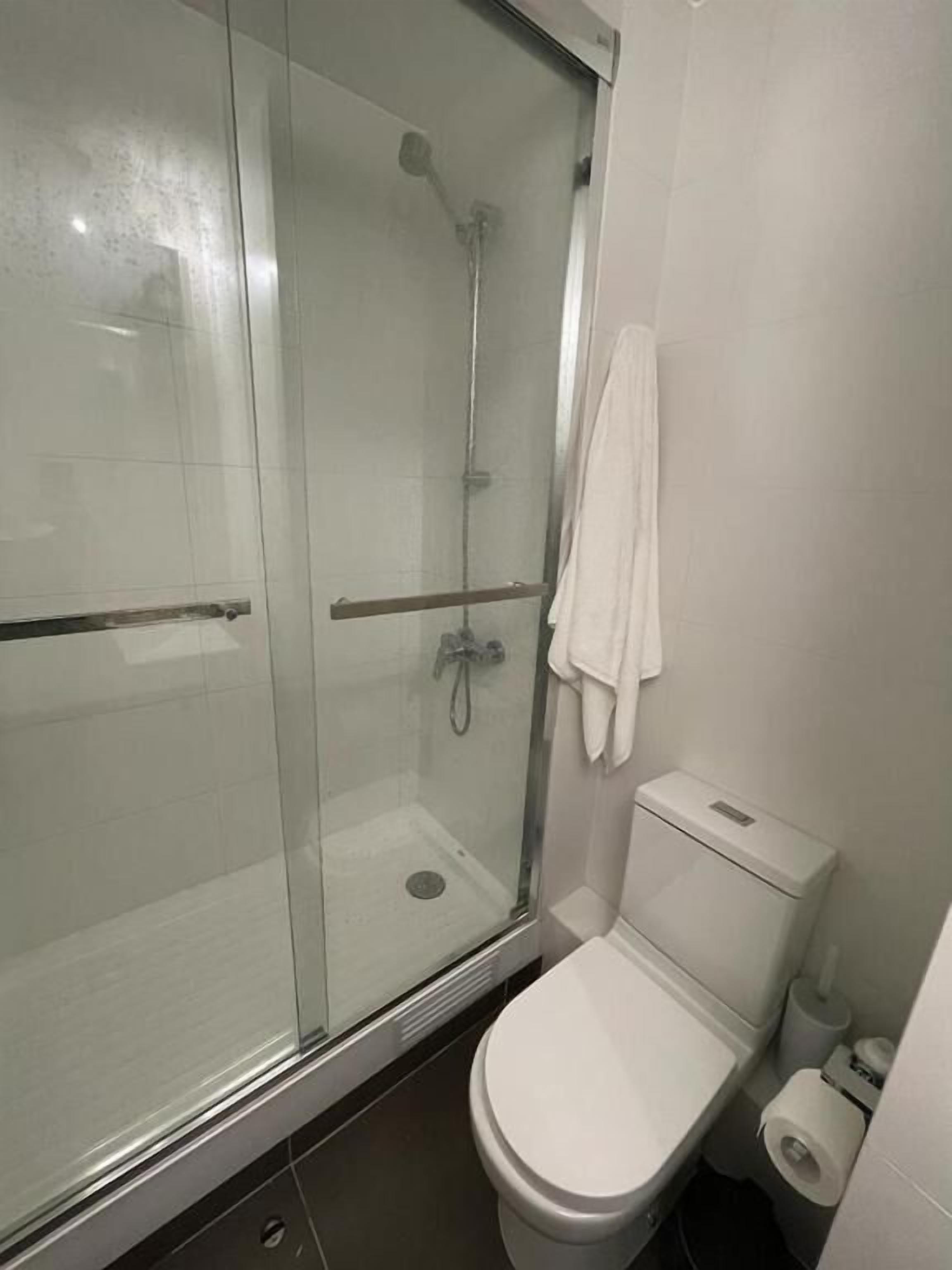 A bathroom with a glass-enclosed shower, a white toilet, and a towel hanging on the wall.