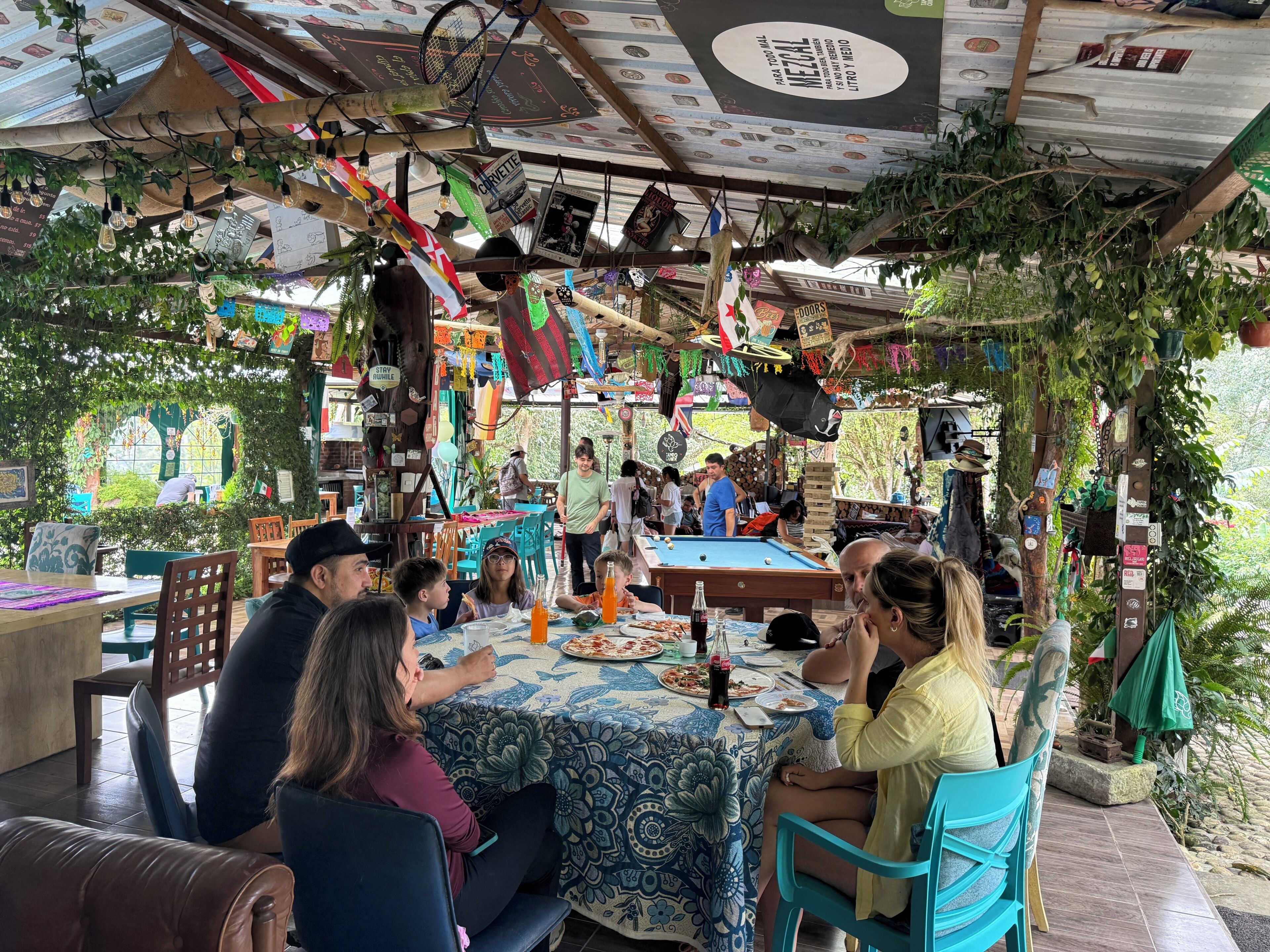 An outdoor dining area with tables and chairs, surrounded by greenery and various decorations.