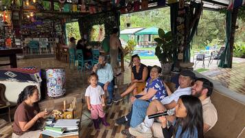 Un grupo de personas sentadas en un sofá y sillas en un espacio exterior cubierto, con un bar y varios objetos en estanterías.