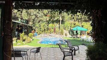 Un patio exterior con piscina, rodeado de follaje y un pabellón.