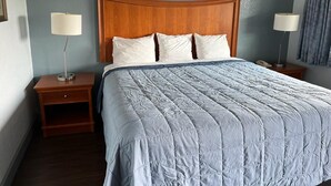 A hotel room with a wooden headboard, a large bed with a quilted bedspread, two bedside tables with lamps, and a nightstand. - Holiday Motel (Jeffersonville)