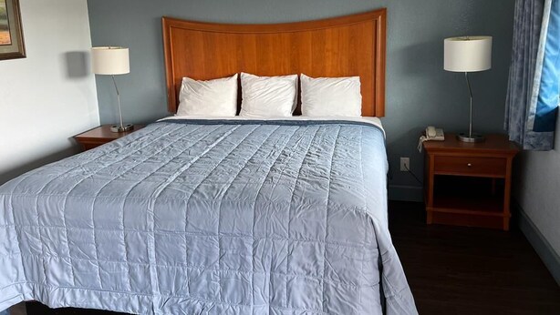 A hotel room with a large bed, two bedside tables, and a nightstand. - Holiday Motel (Jeffersonville)
