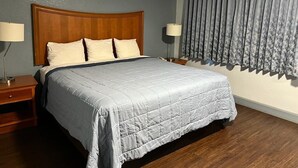 A neatly made bed with a wooden headboard, two bedside lamps, and a window with curtains. - Holiday Motel (Jeffersonville)