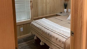 A bedroom with wooden panel walls, a bed with a striped blanket, a ceiling fan, and a window with blinds. - Country Cabin by The Ark (Verona)