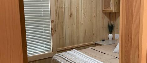 A bedroom with wooden panel walls, a bed with a striped blanket, a ceiling fan, and a window with blinds.