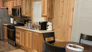 A compact kitchen with wooden cabinets, a microwave, stove, and a dining area with a table and chairs. - Country Cabin by The Ark (Verona)