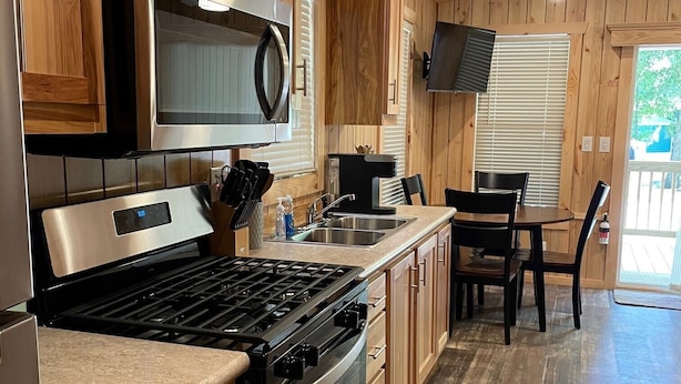 A modern kitchen with wooden cabinets, stainless steel appliances, and a dining area with a table and chairs. - Country Cabin by The Ark (Verona)