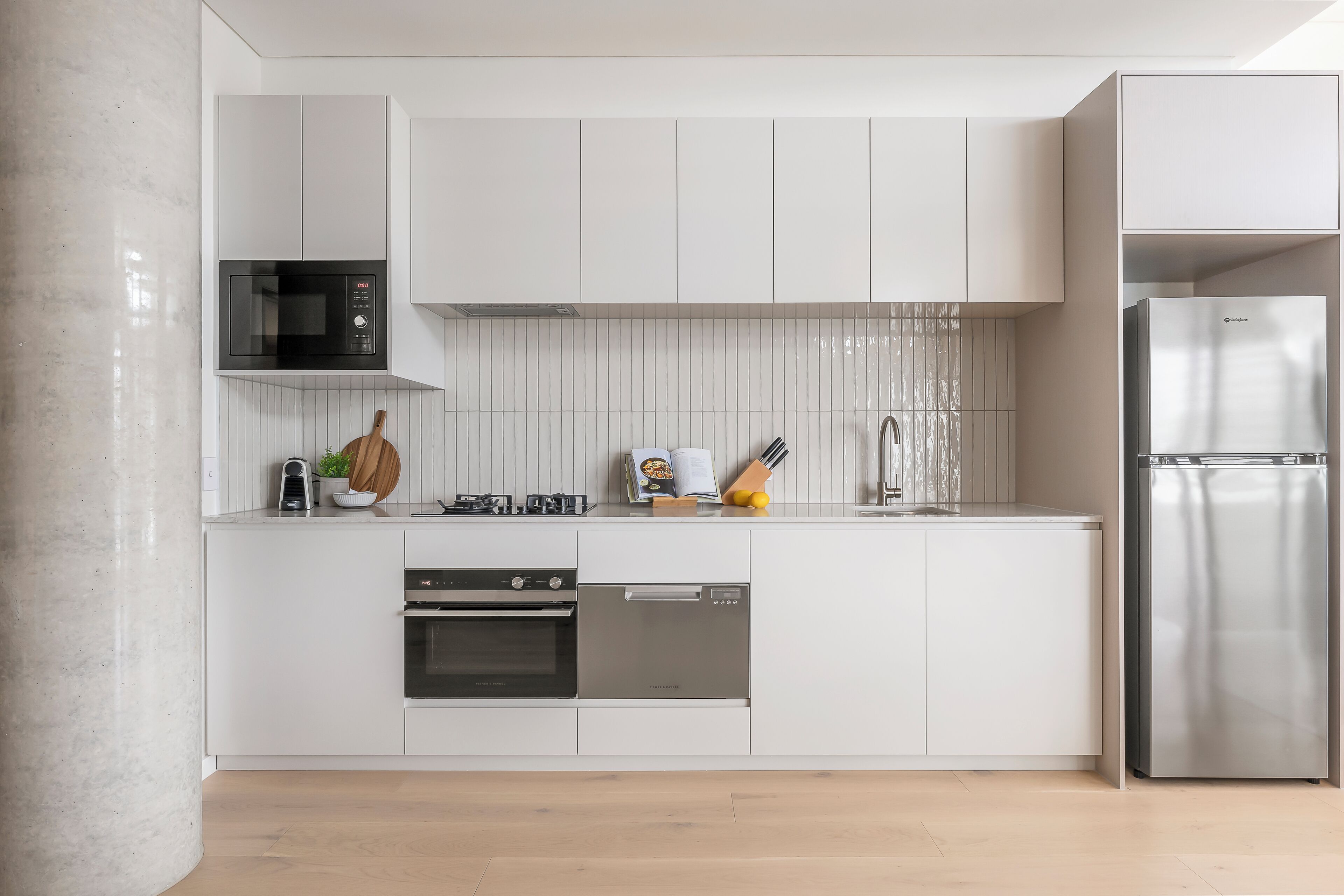 Eine moderne Küche mit weißen Schränken, einem Edelstahl-Kühlschrank, einem Einbauofen und einer Mikrowelle.