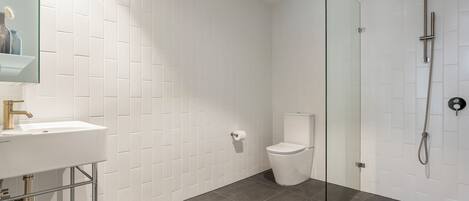 Um banheiro moderno com parede revestida de azulejos brancos, box de vidro, vaso sanitário branco e pia com acessórios cromados.