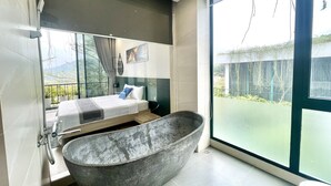 A modern bathroom with a freestanding bathtub, a large window offering a view of the outdoors, and a bed with a view of the balcony.