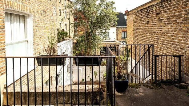 A narrow alleyway with brick buildings, a metal gate, and potted plants.