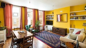 A living room with a wooden dining table, chairs, a sofa, a TV, and bookshelves.