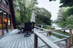Eine Holzterrasse mit Tisch und Stühlen, die auf ein Gewässer blickt und von Bäumen umgeben ist.