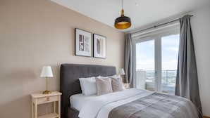 A modern bedroom with a large bed, two bedside tables, a hanging light fixture, and a city view.