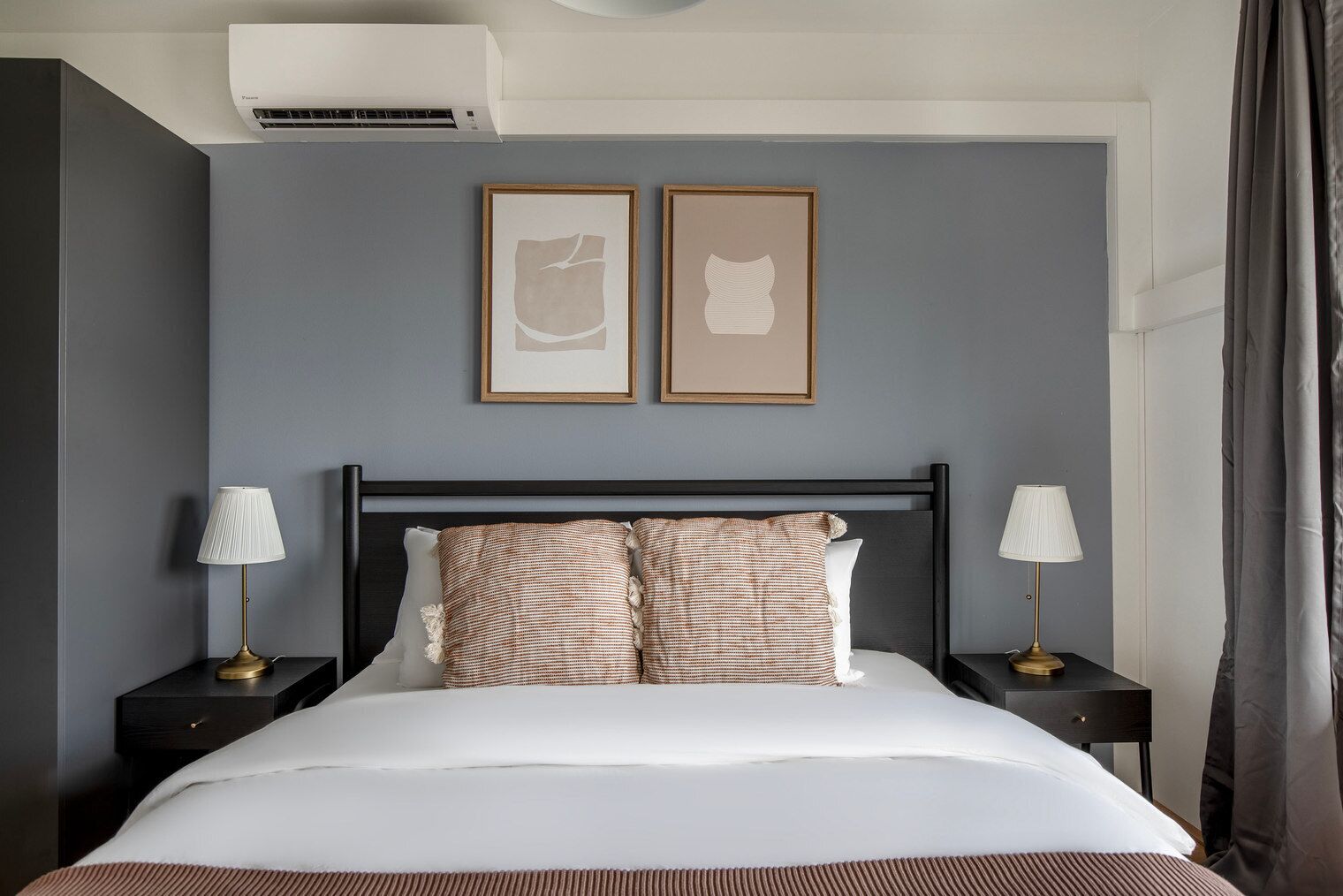 Habitación de hotel ordenada con una cama grande, dos mesitas de noche con lámparas y dos cuadros en la pared.