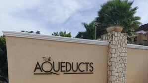 A beige wall with the text "THE AQUEDUCTS" in black, a stone pillar, and a palm tree in the background. - THE AQUEDUCTS OF NEGRIL
"Seaview Paradise" (Negril)