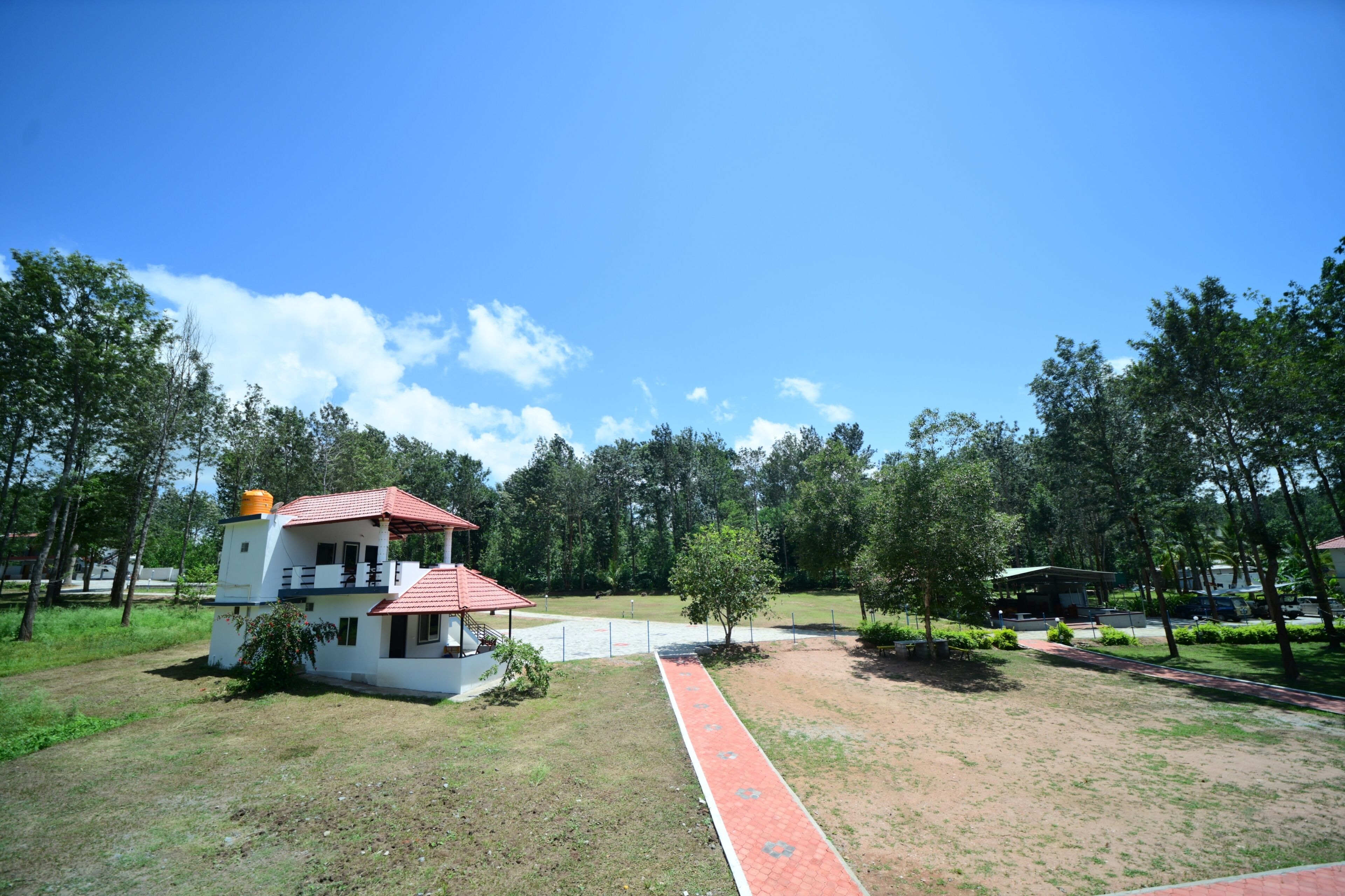 A building with a red roof and white walls, surrounded by trees and a paved walkway.