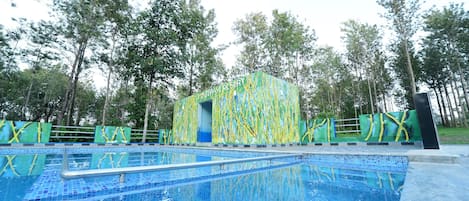 A swimming pool with a blue tiled deck, surrounded by a fence with yellow and green patterns.