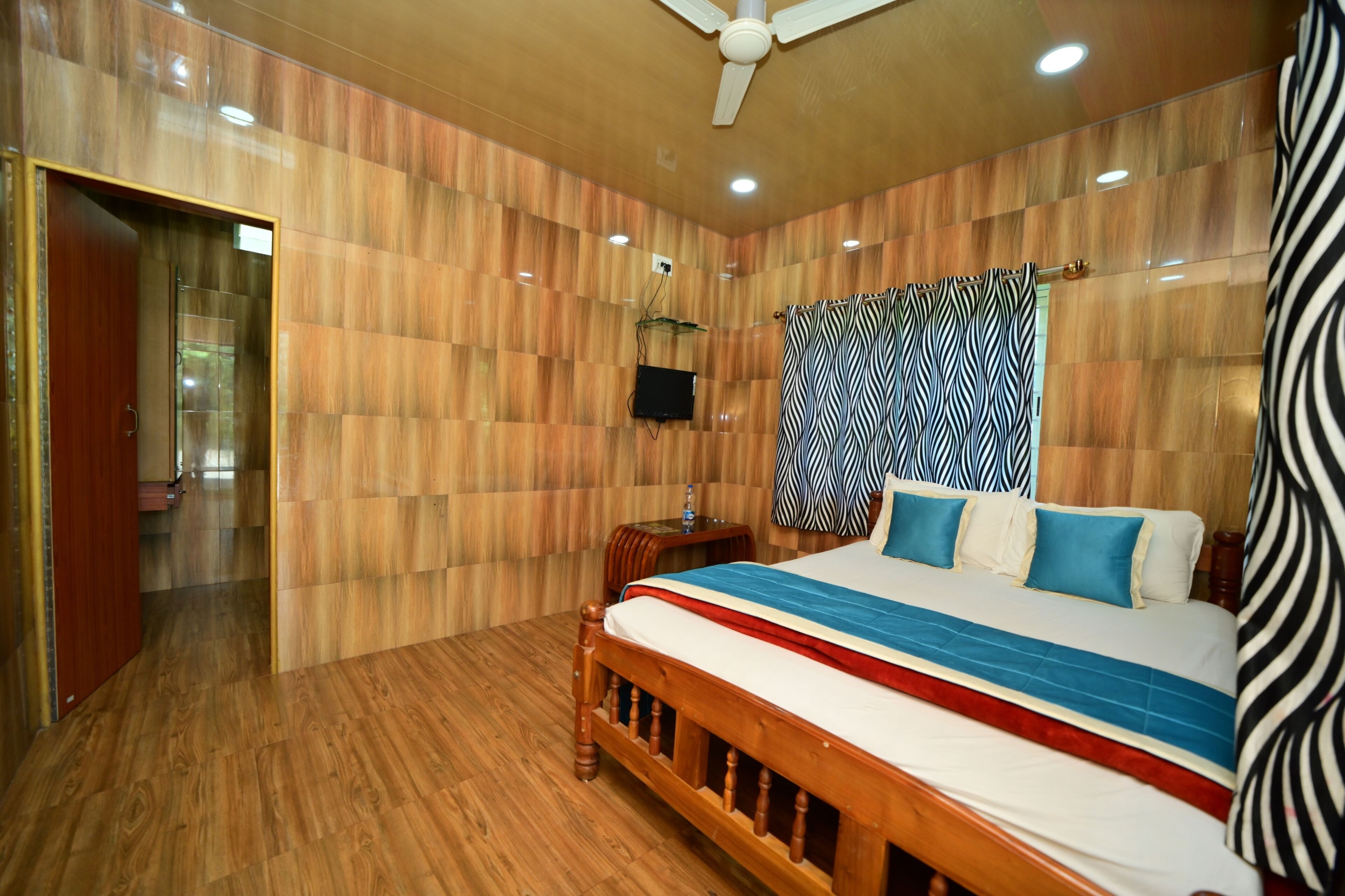 A bedroom with a wooden floor, a bed with a striped bedspread, a ceiling fan, and a television on a wooden stand.